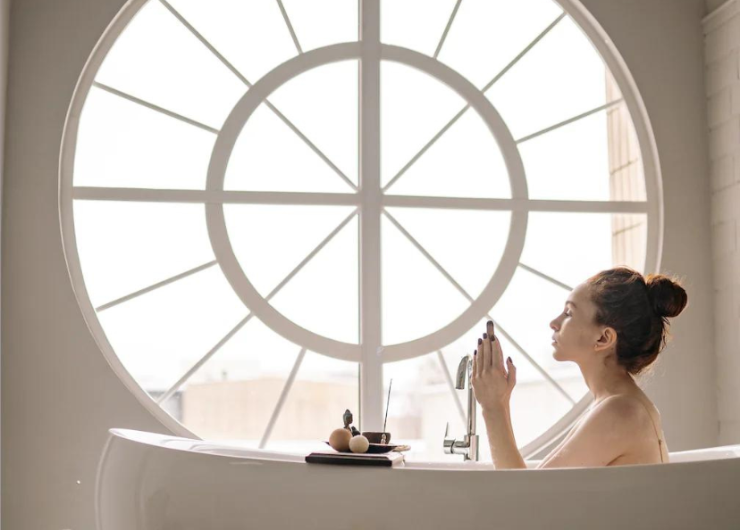 Woman in a bathtub with a large round window in the background.